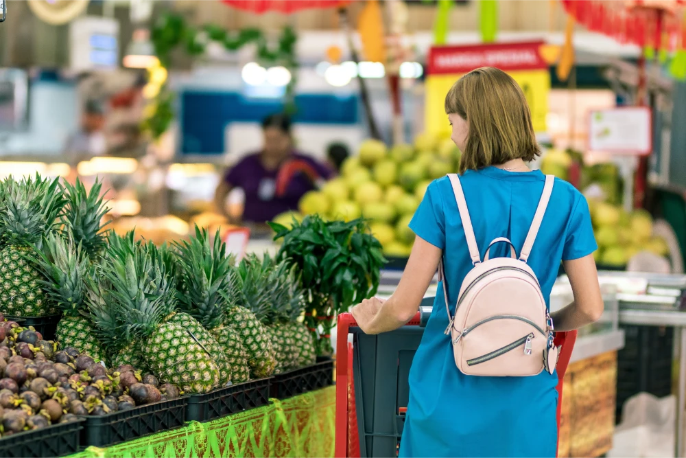 Woman shopping in supermarket aisle with pineapples and shopping cart, illustrating supermarket accident risks.